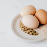 Three fresh eggs on a decorative plate with feathers on a white background.